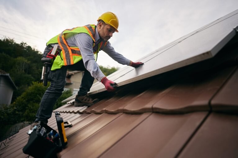 Low angle view of professional worker covering roof with solar panels. Copy space.